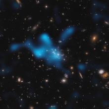 Ghostly clouds of hot gas glow bright blue against a background of many distant galaxies